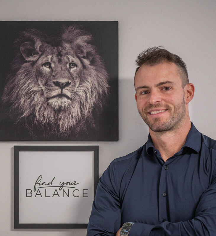 Mann in dunkelblauem Hemd steht vor Wand mit Löwenbild und Schriftbild 'find your BALANCE'.